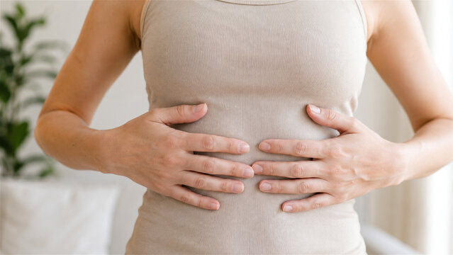 woman holding her abdomen with both hands because of stomach pain. Closeup home scene suggests digestive discomfort and concern. Healthcare concept for symptom awareness