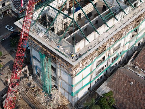 Aerial view of the construction site of the Wangaya Regional General Hospital Emergency Room with a red crane and steel roof framework in Denpasar Utara, Bali, Indonesia.
