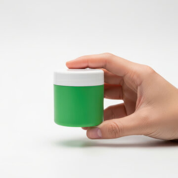 A hand holding a small green plastic container with a white lid