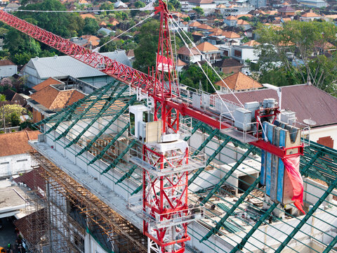 Aerial view of the construction site at Wangaya Regional General Hospital, featuring a red tower crane over a building with a green roof frame in Kecamatan Denpasar Utara, Bali, Indonesia.