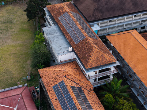 Aerial view of SMKN 1 Denpasar featuring terracotta tiled roofs with integrated solar panels, surrounded by lush greenery and school grounds in Kecamatan Denpasar Utara, Bali, Indonesia.