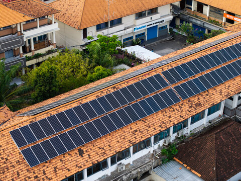 Aerial view of SMKN 1 Denpasar featuring solar panels installed on the terracotta tiled roof of the school building in Kecamatan Denpasar Utara, Bali, Indonesia.