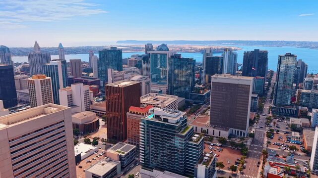 Dense cluster of modern glass skyscrapers defining the city's central business district. Calm waters of the harbor and the low-lying peninsula of Coronado in the distance. San Diego, California, USA.