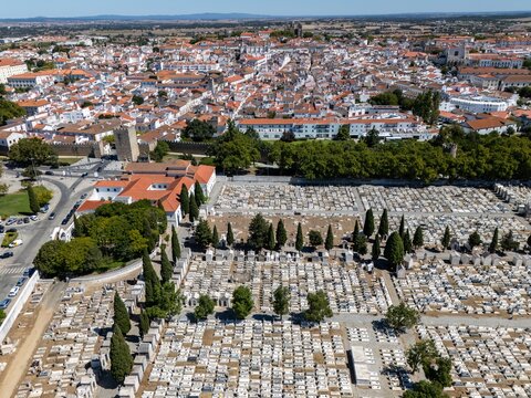 Aerial view of the cemetery with rows of white tombs and cypress trees, situated next to the historic city center of Evora, Evora District, Portugal.