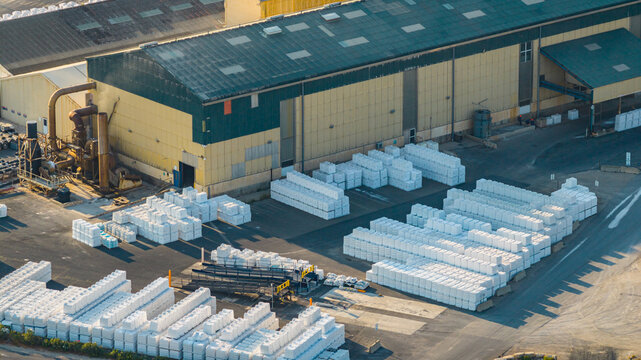 Aerial view of large outdoor sea salt storage yard with thousands of packaged salt bags stacked beside an industrial processing warehouse in Aigues-Mortes, Occitanie, France.