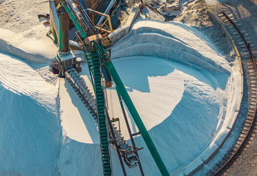 Aerial view of industrial salt stockpile handling machinery and conveyor system at a sea salt processing facility in the Camargue region, Aigues-Mortes, Occitanie, France.