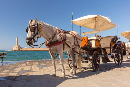Traditional horse-drawn carriage on the waterfront of Chania with the lighthouse and Mediterranean Sea in the background, Crete, Greece.