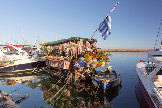 Floating souvenir shop displaying jewelry and handmade goods among moored boats in Chania harbor, Crete, Greece.