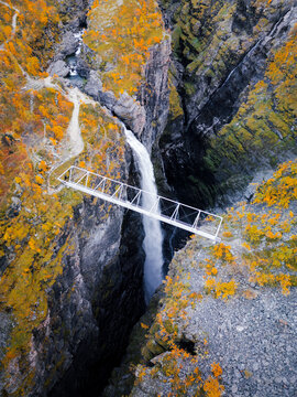 Aerial view of Gorsa bridge spanning a deep canyon with a powerful waterfall, surrounded by vibrant autumn foliage and rugged rocky cliffs in Birtavarre, Troms, Norway.
