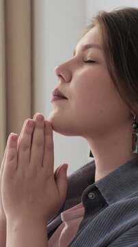 Woman praying with folded hands and closed eyes, concept of faith, spirituality, devotion, hope, contemplation and inner peace, Vertical Video.