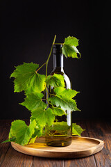 Elegant bottle of white wine with fresh green vine leaves on a rustic wooden surface © thayra83
