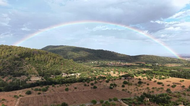 Hope and renewal concept wide aerial view of a vibrant rainbow arching over a green valley and rolling hills after a rainstorm cinematic drone shot