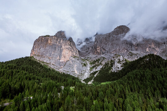 Castelrotto, Italy - 19 August 2024: Aerial view of Val Gardena with dramatic limestone peaks, dense coniferous forests, and low-hanging clouds in the Dolomites.