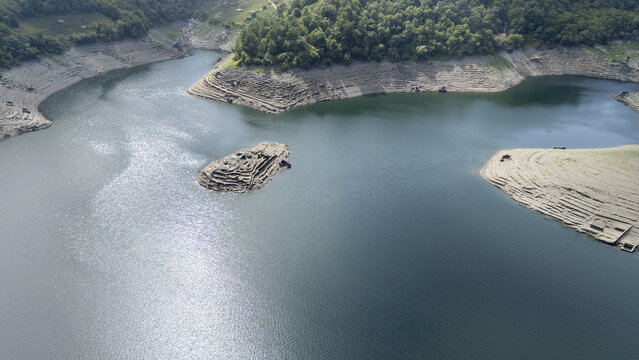 Aerial view of the historic Castro Candaz archaeological site emerging from the waters of the Mino River, surrounded by terraced hills and lush forests in Belesar, Lugo, Spain.