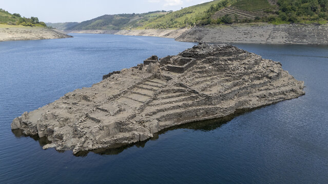 Aerial view of Castro Candaz, an ancient hillfort ruin emerging from the waters of the Mino River, surrounded by terraced hillsides in Belesar, Lugo, Spain.