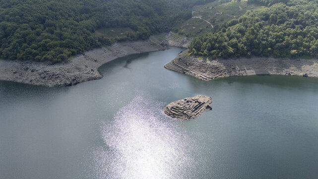 Aerial view of the Castro Candaz archaeological site in the Mino river reservoir, surrounded by lush green hills and sunlight reflecting on the water in Belesar, Lugo, Spain.