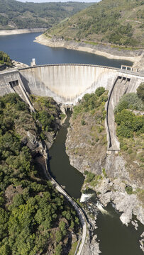 Aerial view of the Encoro de Belesar dam spanning the Mino River, surrounded by lush green hills and rocky cliffs in Lugo, Lugo, Spain.
