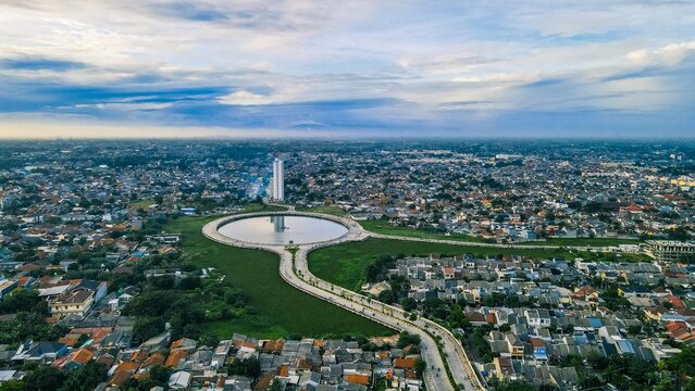 Aerial view of the circular lake and surrounding urban landscape with a tall building in Bekasi Barat, West Java, Indonesia.