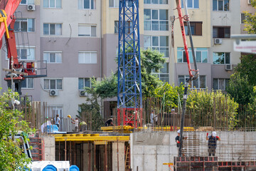Construction workers poured concrete into reinforced building structures using a large pump boom and tower crane in an urban development zone. © Andrey