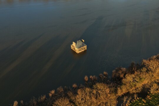 Coueron, France - 29 December 2025: Aerial view of La Maison dans la Loire, an art installation house partially submerged in the Loire River, surrounded by calm water and riverbank vegetation.
