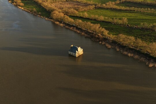 Coueron, France - 29 December 2025: Aerial view of La Maison dans la Loire, an art installation house partially submerged in the Loire River, surrounded by calm water and green banks.