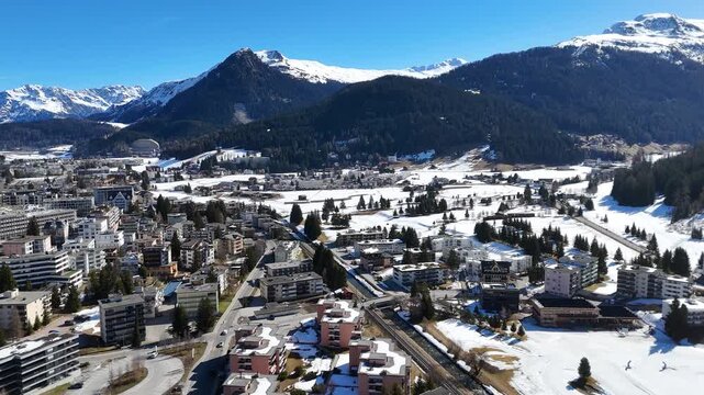 davos town spreads across landwasser valley switzerland railway line threads center mountain ranges rise snowcapped peaks forested slopes flank valley aerial drone footage wide establishing clear sky