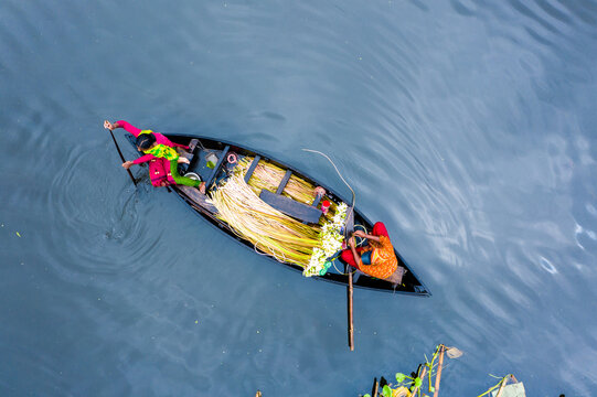 Munshiganj, Bangladesh - 01 August 2021: Aerial view of two people in a wooden boat transporting harvested jute fibers across the calm river water.