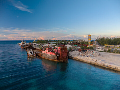 Nassau, The Bahamas - 16 September 2026: Aerial view of Arawak Cay featuring rusted shipwrecks moored along the dock, turquoise Caribbean waters, and a storage silo under a clear sky.