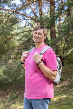 Smiling Caucasian man in his 40s looking at camera with backpack in pine forest in sunlight