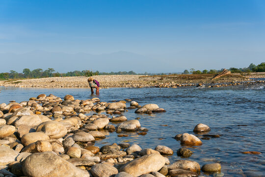 Fisherman trying to catch fishes on Murti river in the morning, riverbed in foreground stones. Scenic beauty of Dooars landscape, West Bengal, India. Dooars is popular tourist destination.