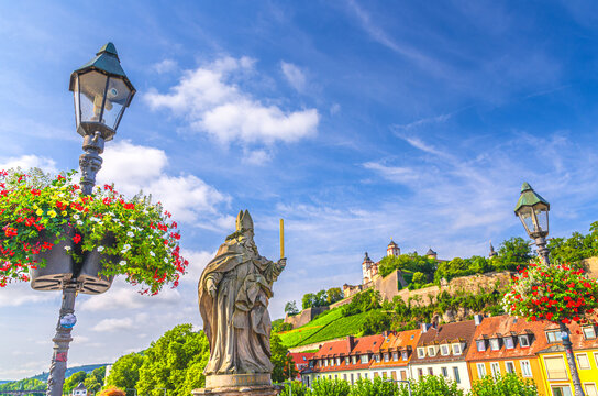 Wurzburg, Germany, July 14, 2024: Br&uuml;ckenstatue Saint Burkard statue on Old Main Bridge, Marienberg Fortress and castle wall on Mary's Mount hill with vineyards in Wurzburg old town, Bavaria state