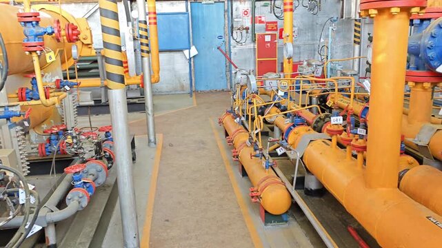 Industrial control equipment dominates this plant room, where orange manifolds, blue housings and pressure gauges line up for monitoring. Machinery network feels precise and highly engineered.