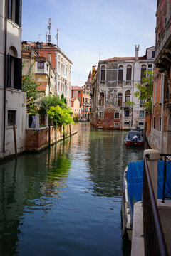 A quiet Venetian canal reflecting historic buildings, with a moored boat and distant bell tower under a clear sky.