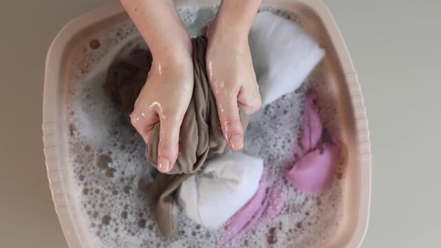 Person hand washing clothes in soapy water, household laundry and fabric care concept