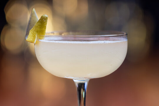 Elegant cocktail, the Bees Knees in coupe glass. Lemon twist adorns the rim. Warm wood table. Perfect for bar, lounge