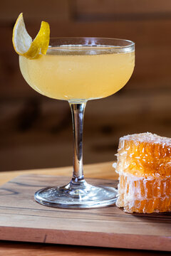 Elegant cocktail, the Bees Knees in coupe glass. Lemon twist adorns the rim. Warm wood table and honey comb garnish.