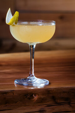 Elegant cocktail, the Bees Knees in coupe glass. Lemon twist adorns the rim. Warm wood table. Perfect for bar, lounge