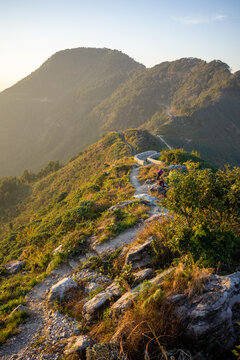 Hikers walk along a scenic rocky ridge trail through green hills at golden hour near Bandipur, Nepal.