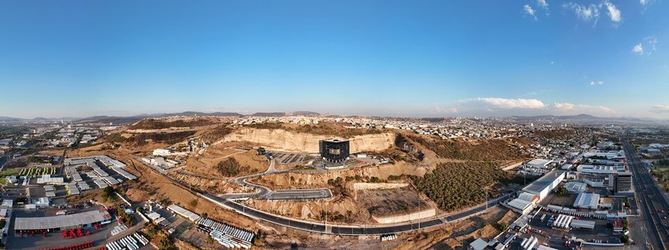 Santiago de Queretaro, Mexico - 14 September 2026: Aerial view of BLOQUE - Centro de Innovacion y Tecnologia Creativa, a modern black building on a hillside overlooking the city and industrial area.