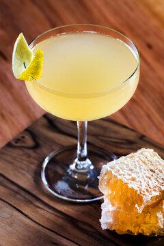 Elegant cocktail, the Bees Knees in coupe glass. Lemon twist adorns the rim. Warm wood table and honey comb garnish.