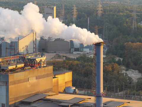 Genk, Belgium - 27 August 2026: Aerial view of the industrial site in Genk Zuid, featuring a smoke stack emitting steam amidst heavy industrial infrastructure, power lines, and forest.