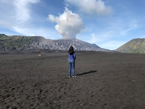A woman standing on the vast volcanic sand dunes of Mount Bromo in Indonesia.