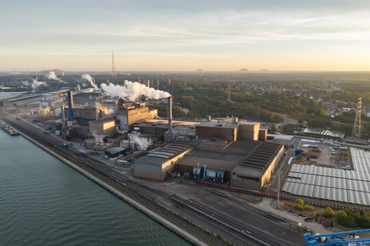 Genk, Belgium - 27 August 2026: Aerial view of the industrial facilities at Genk Zuid, featuring manufacturing buildings, smoking chimneys, and canal-side infrastructure under a sunset sky.
