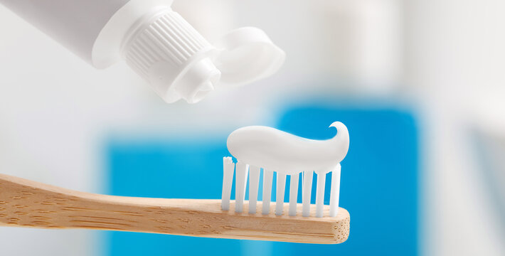 Toothpaste on toothbrush and tube against blurred background, closeup. Banner design