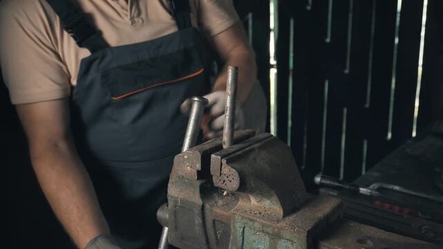 Male technician in gray workwear adjusts metal rod in a vise, demonstrating a precise action sequence in a workshop with tools and equipment visible in the background