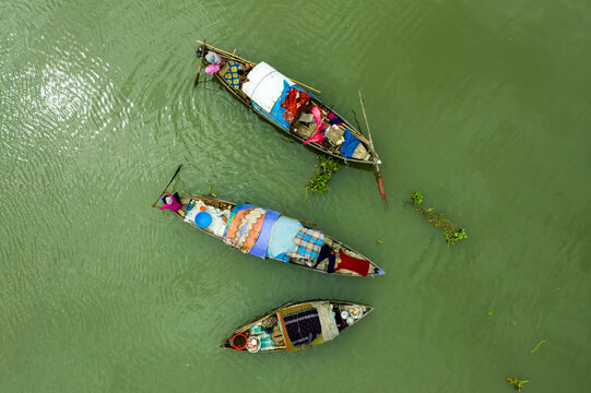 Dhaka, Bangladesh - 17 October 2021: Aerial view of three traditional wooden boats navigating the green river water with people on board.