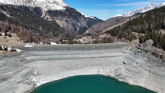 marmorera dam rockfill embankment holds back turquoise reservoir alpine hamlet rooftops nestle valley floor beyond crest road snowcapped peaks forested slopes frame julier pass graubunden switzerland