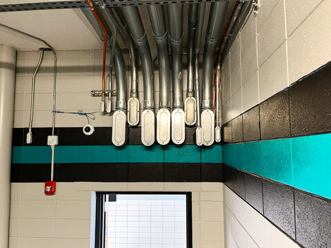Electrical conduits on a cement block wall with bold vertical stripes.