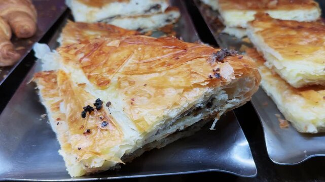 Crispy baked burek pie displayed on metal trays in a bakery setting