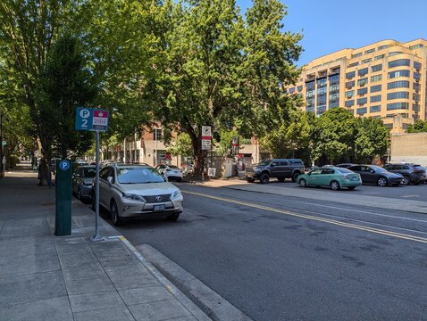 Portland, Oregon, USA - July 18, 2024: Tree-lined downtown street with parked cars and parking signs
